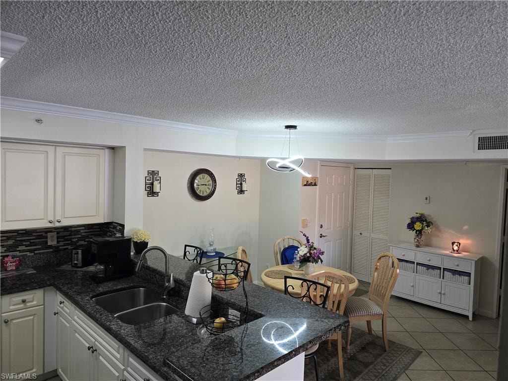 Kitchen featuring a textured ceiling, a sink, a peninsula, ornamental molding, and light tile patterned flooring