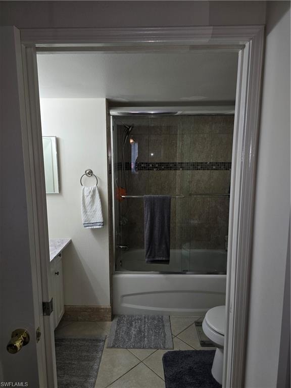 Full bath featuring tile patterned flooring, vanity, toilet, baseboards, and combined bath / shower with glass door