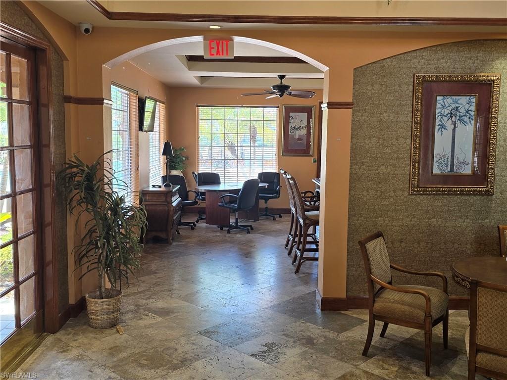 Office with baseboards, ceiling fan, stone finish floor, a raised ceiling, and arched walkways