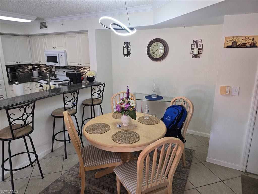 Dining room with an inviting chandelier, ornamental molding, light tile patterned floors, and visible vents