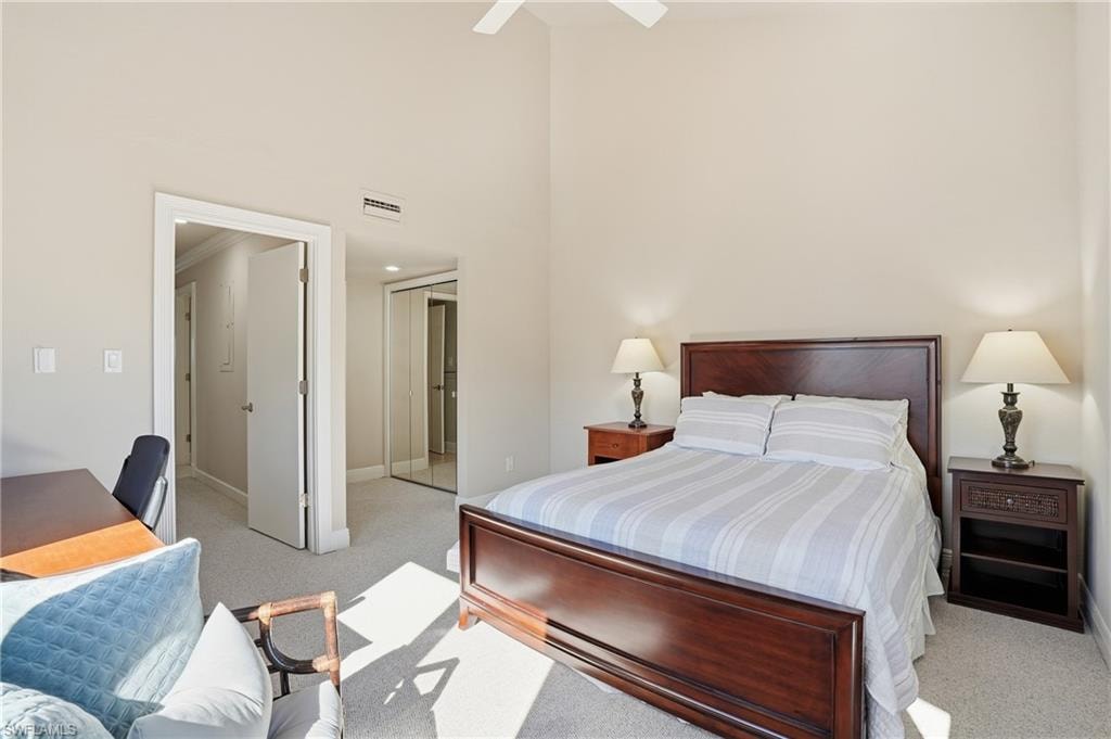Bedroom featuring a closet, light colored carpet, a high ceiling, a ceiling fan, and a desk