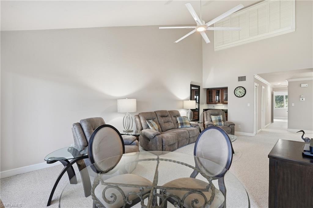 Living area featuring a towering ceiling, light colored carpet, a ceiling fan, and ornamental molding