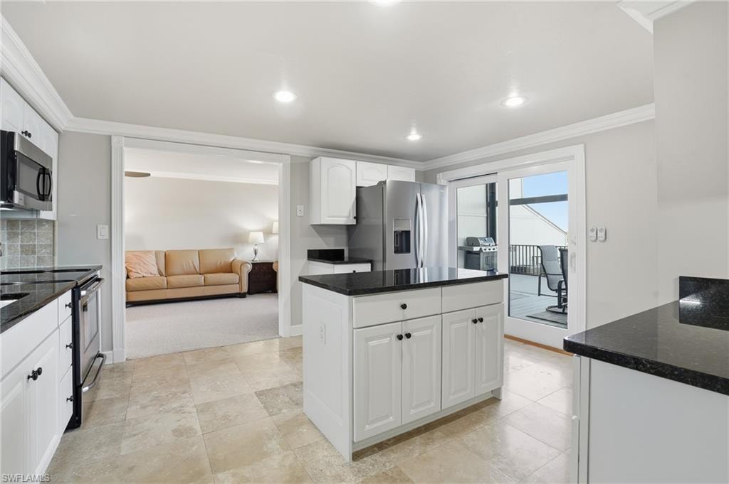 Kitchen with crown molding, white cabinetry, dark stone countertops, appliances with stainless steel finishes, and a center island
