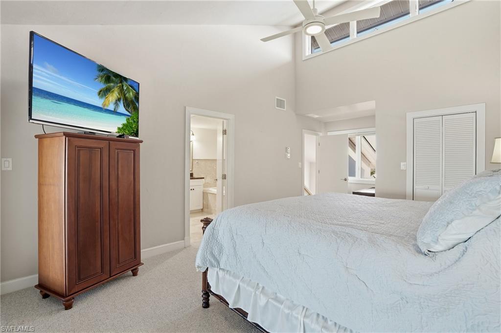 Bedroom with light colored carpet, a ceiling fan, a towering ceiling, ensuite bath, and a closet