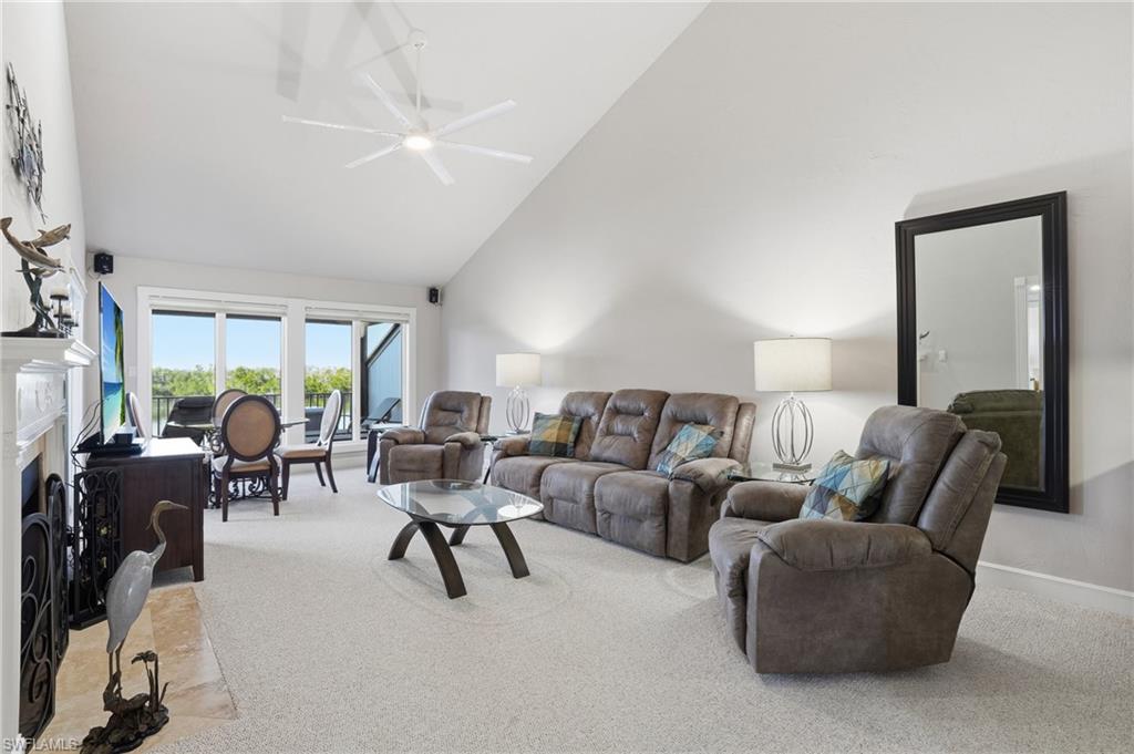 Carpeted living area with high vaulted ceiling, a fireplace, and ceiling fan