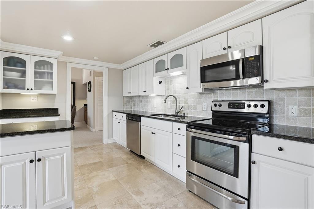 Kitchen with stainless steel appliances, glass insert cabinets, dark stone counters, ornamental molding, and recessed lighting