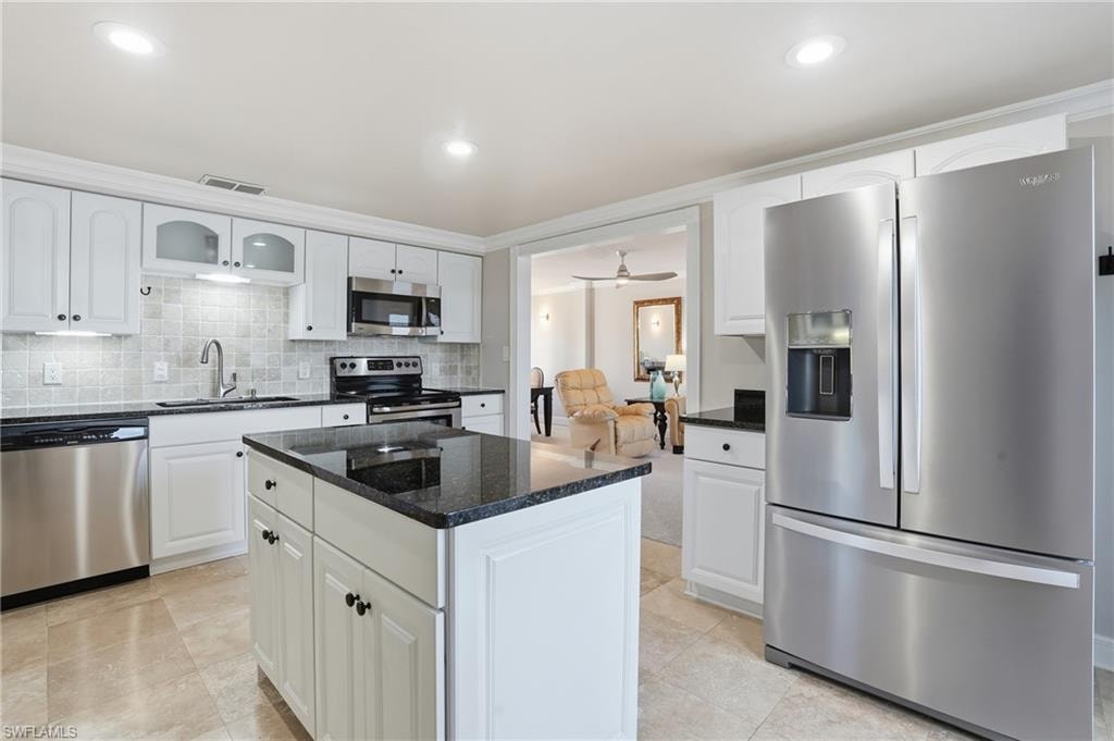 Kitchen with stainless steel appliances, dark stone counters, white cabinets, a ceiling fan, and backsplash