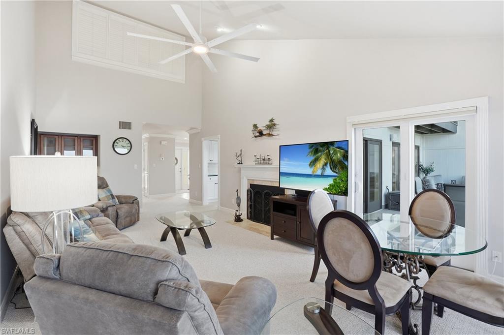 Carpeted living area featuring a fireplace with flush hearth, a high ceiling, and ceiling fan