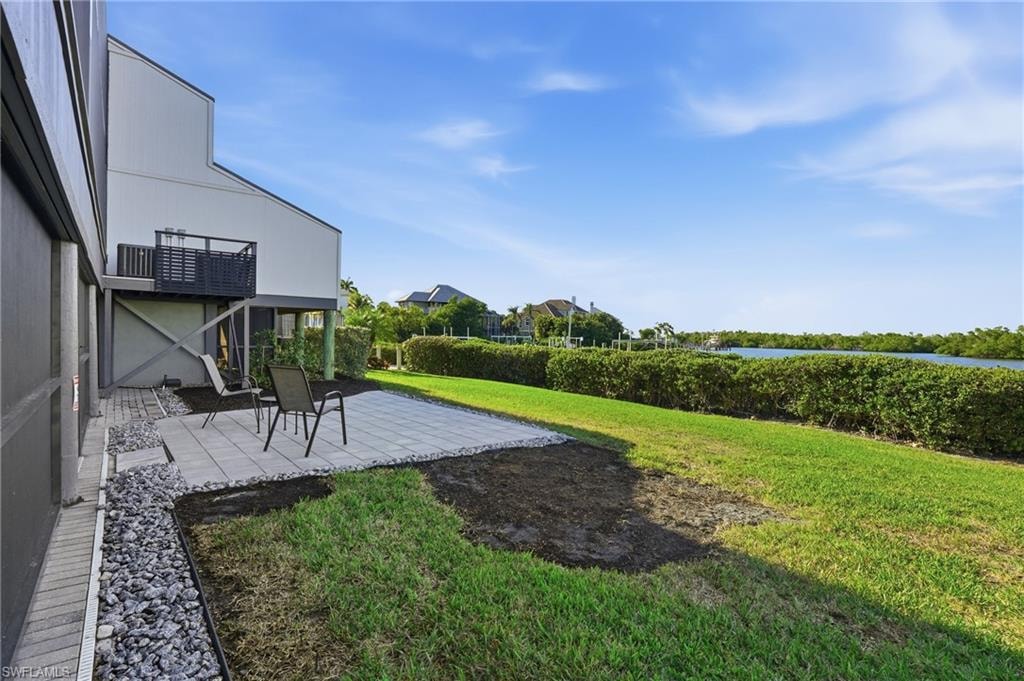 View of green lawn featuring a water view and a patio area