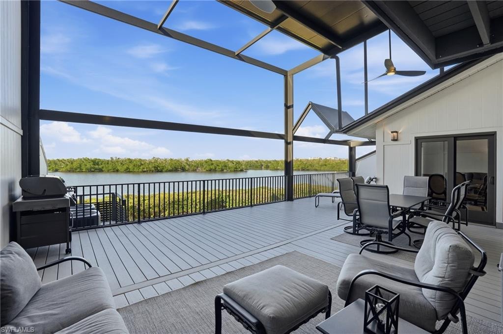 View of patio featuring a sunroom, grilling area, glass enclosure, outdoor dining space, and a water view