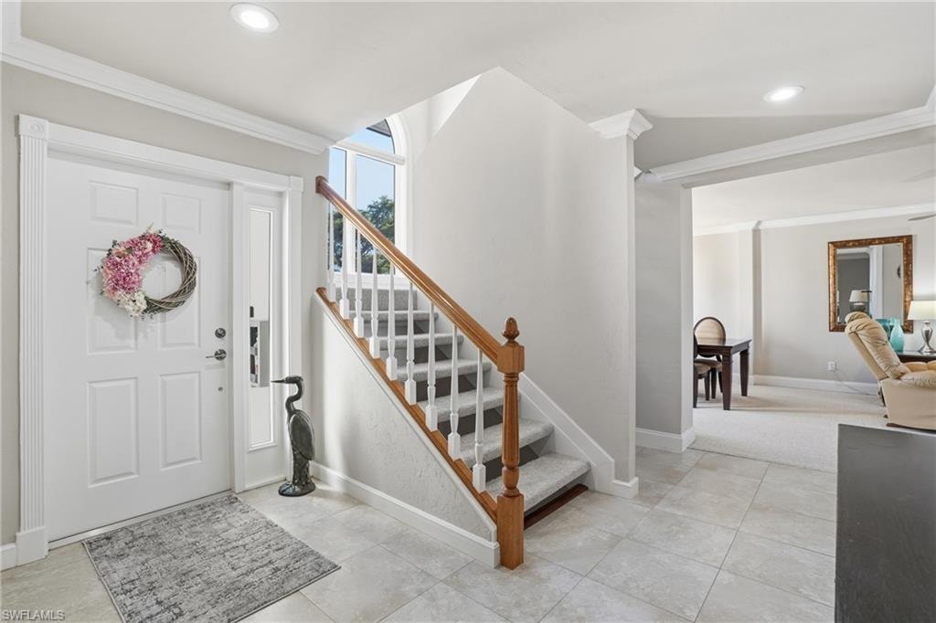 Foyer entrance with crown molding, recessed lighting, light tile patterned floors, and stairs