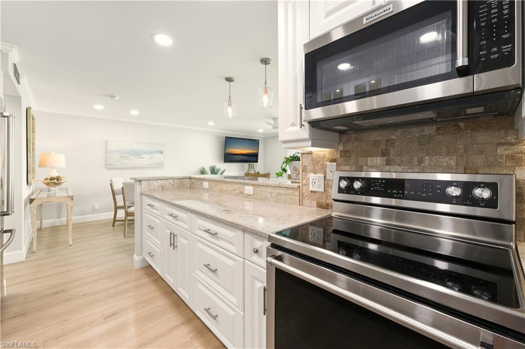 Kitchen featuring stainless steel   appliances, white cabinets, crown molding, light stone countertops, and light vinyl finished floors