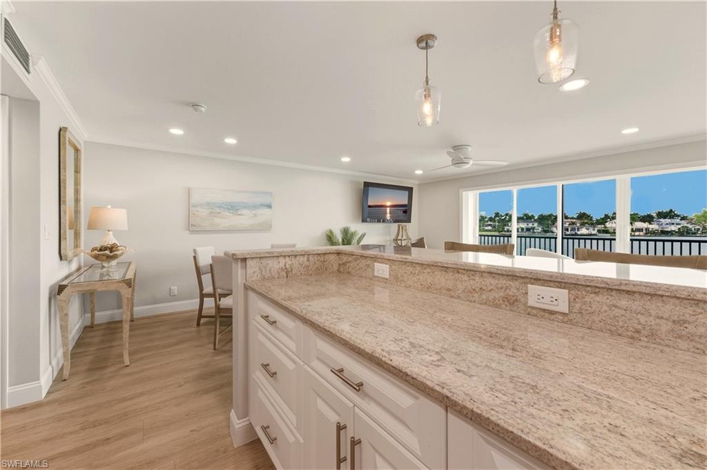 Kitchen with light stone countertops, pendant lighting, white cabinetry, light vinyl floors, and ornamental molding