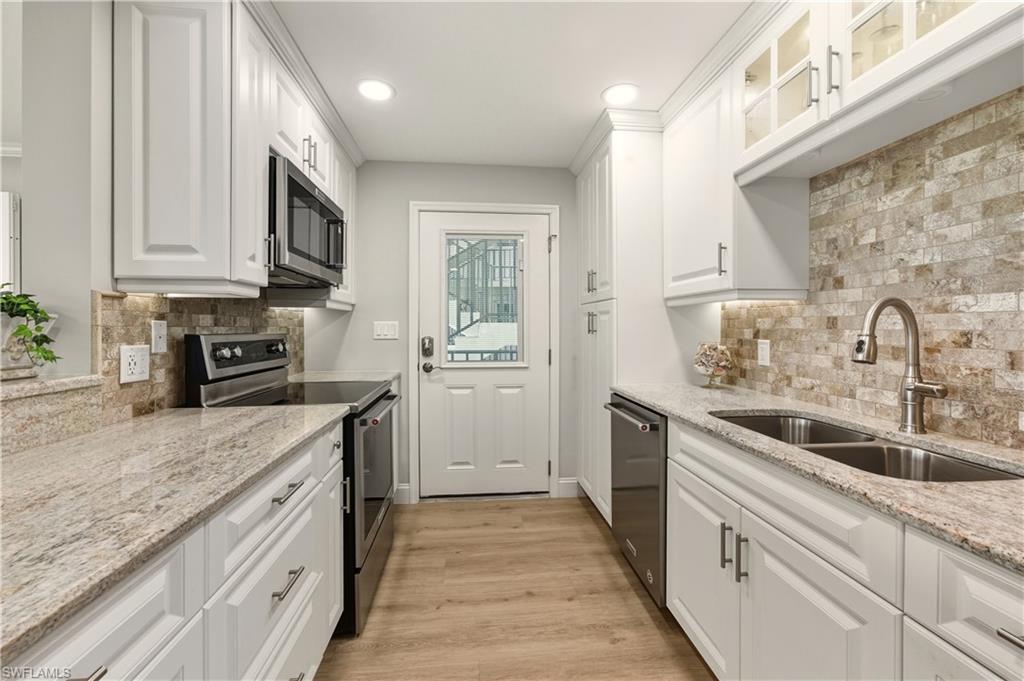 Kitchen featuring appliances with stainless steel finishes, white cabinetry, light stone countertops, light wood-style flooring, and recessed lighting