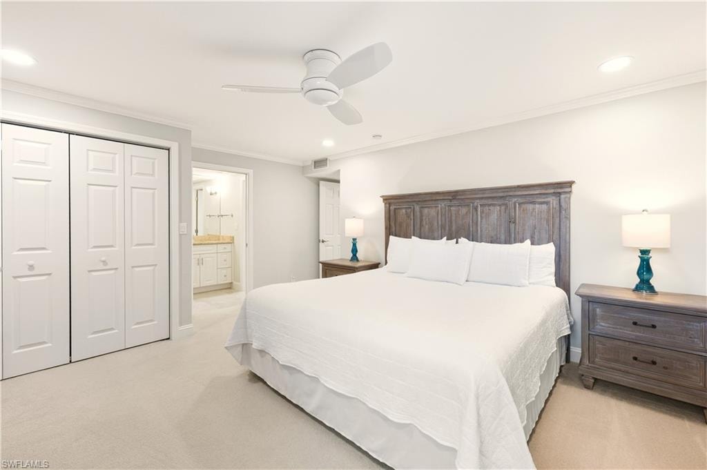 Bedroom with ornamental molding,             ceiling fan, light colored carpet, connected bathroom, and a closet