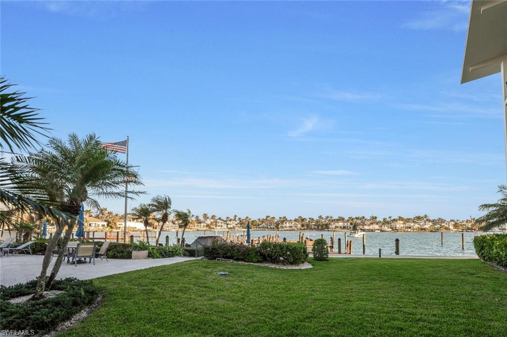 View of green lawn with a dock, a water view, and a patio area
