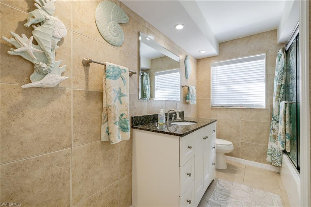 Bathroom featuring tile walls, vanity, recessed lighting, shower / bath combo with shower curtain, and light tile patterned flooring