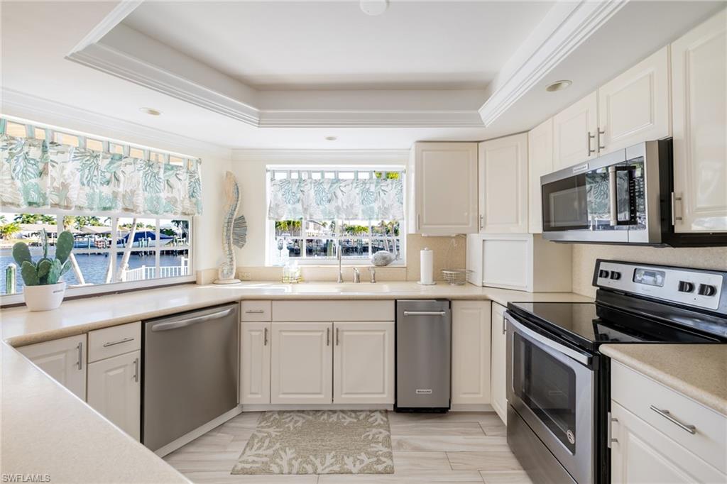 Kitchen featuring appliances with stainless steel finishes, light countertops, white cabinets, and ornamental molding