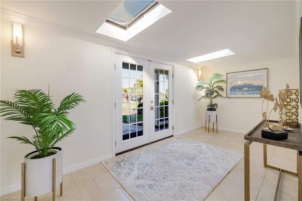 Entrance foyer featuring french doors, ornamental molding, a skylight, and light tile patterned floors