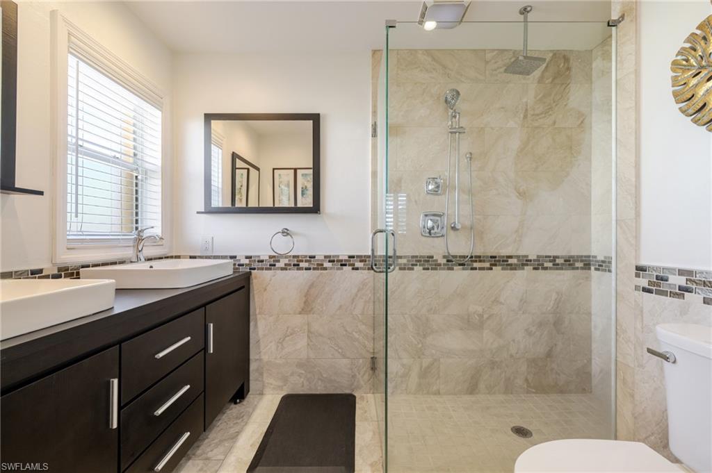 Full bathroom featuring double vanity, a shower stall, tile walls, and a wainscoted wall