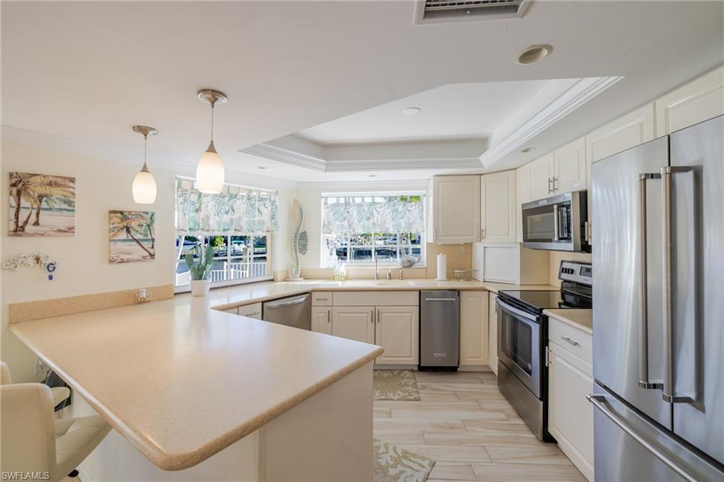 Kitchen featuring ornamental molding, stainless steel appliances, light countertops, decorative light fixtures, and a peninsula