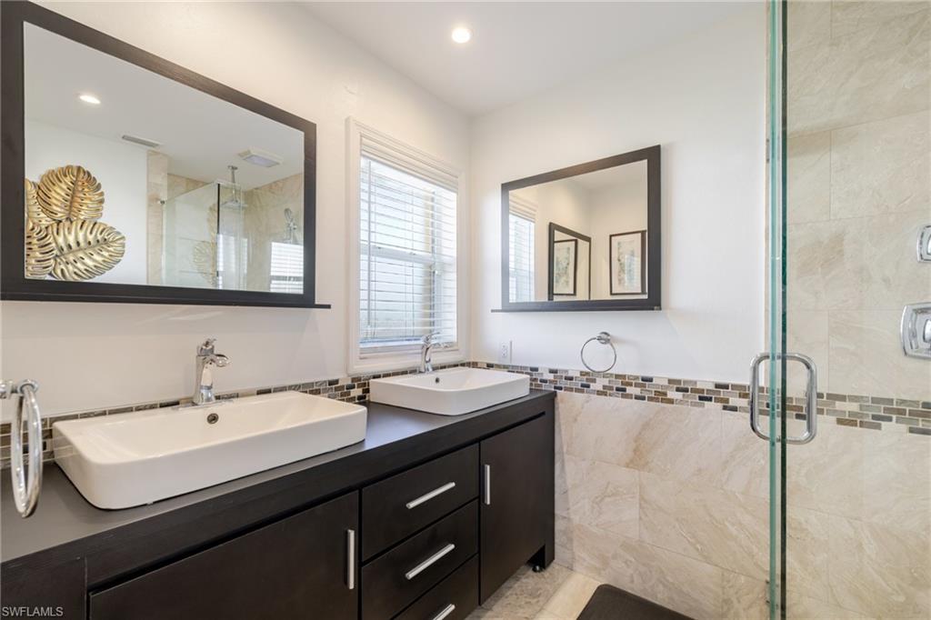Full bath featuring a shower stall, double vanity, and tile walls