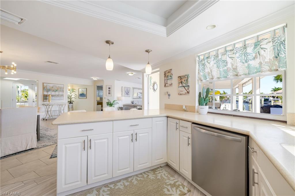 Kitchen with stainless steel dishwasher, open floor plan, pendant lighting, ornamental molding, and white cabinetry