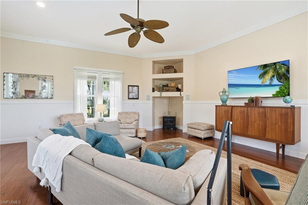 Living area with a wainscoted wall, built in features, wood finished floors, ceiling fan, and ornamental molding