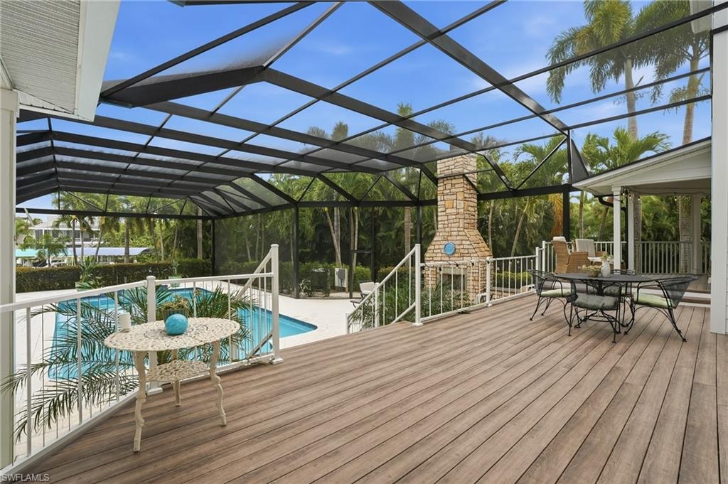 Wooden deck with a lanai, an outdoor fireplace, a sunroom, outdoor dining area, and an outdoor pool