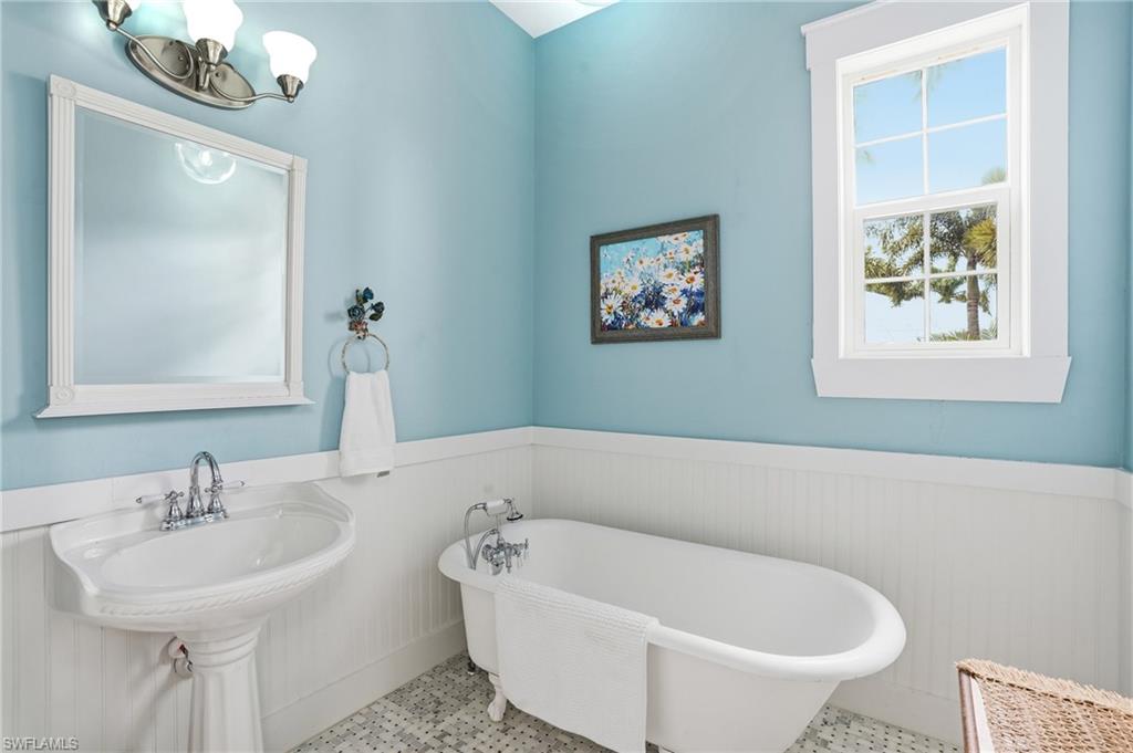 Bathroom featuring wainscoting, a soaking tub, and a chandelier