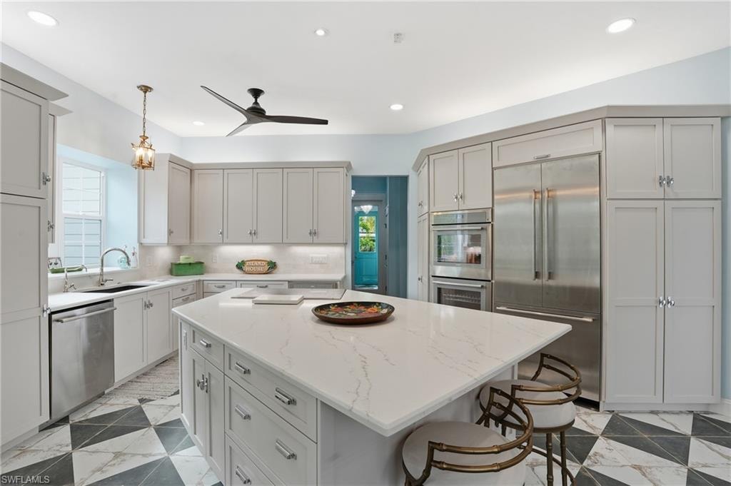 Kitchen featuring appliances with stainless steel finishes, light stone counters, decorative light fixtures, a kitchen island, and a kitchen bar