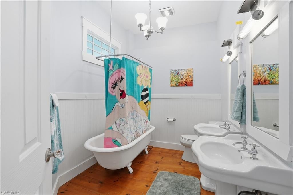 Full bath featuring a wainscoted wall, hardwood / wood-style flooring, a chandelier, and a combined bath / shower with freestanding tub