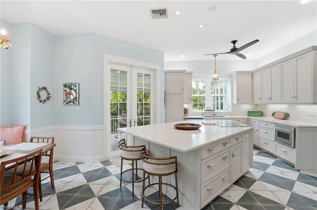 Kitchen with hanging light fixtures, french doors, wainscoting, a kitchen bar, and a center island