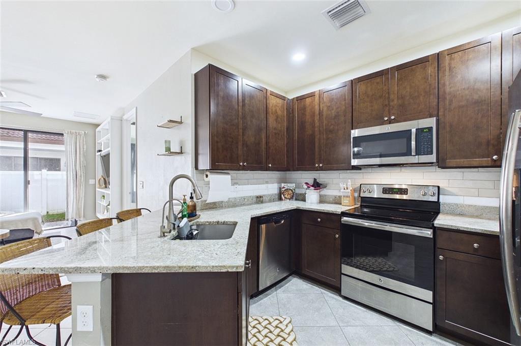 Kitchen featuring appliances with stainless steel finishes, a breakfast bar, dark brown cabinets, a peninsula, and light stone countertops