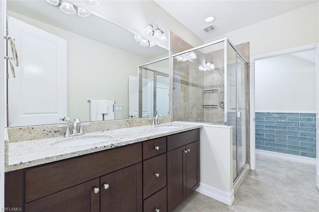 Full bath featuring double vanity, a shower stall, a wainscoted wall, and light tile patterned floors