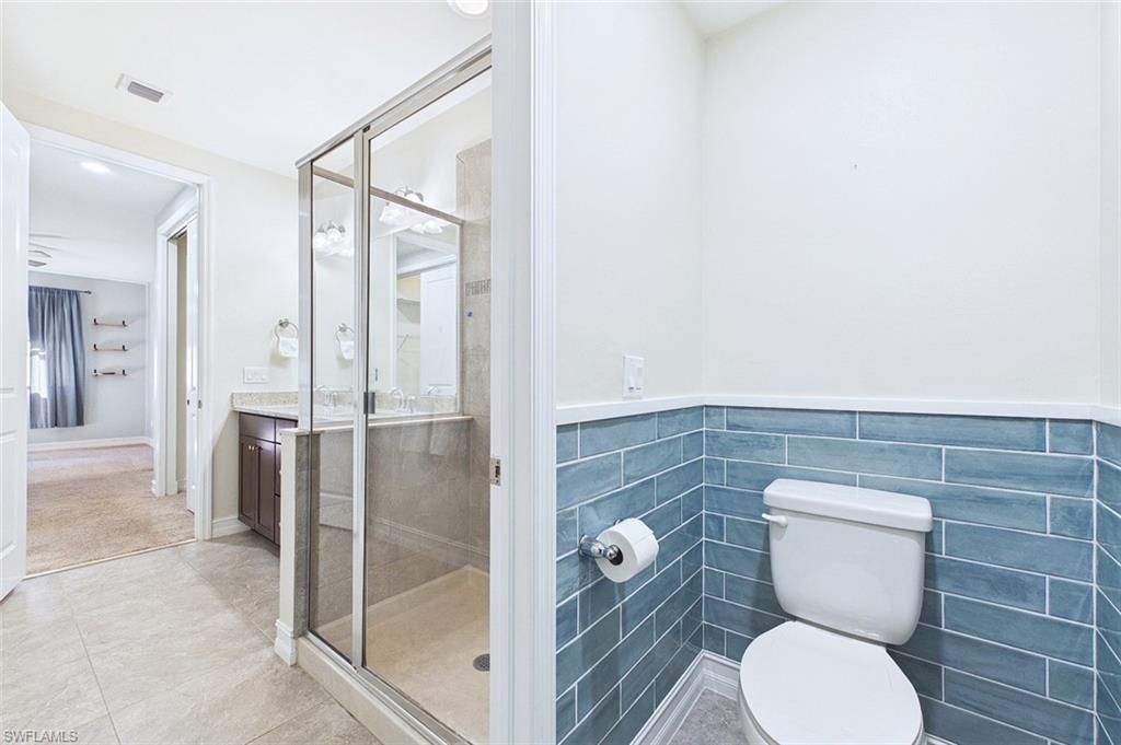Full bathroom with vanity, a shower stall, wainscoting, tile walls, and light tile patterned floors