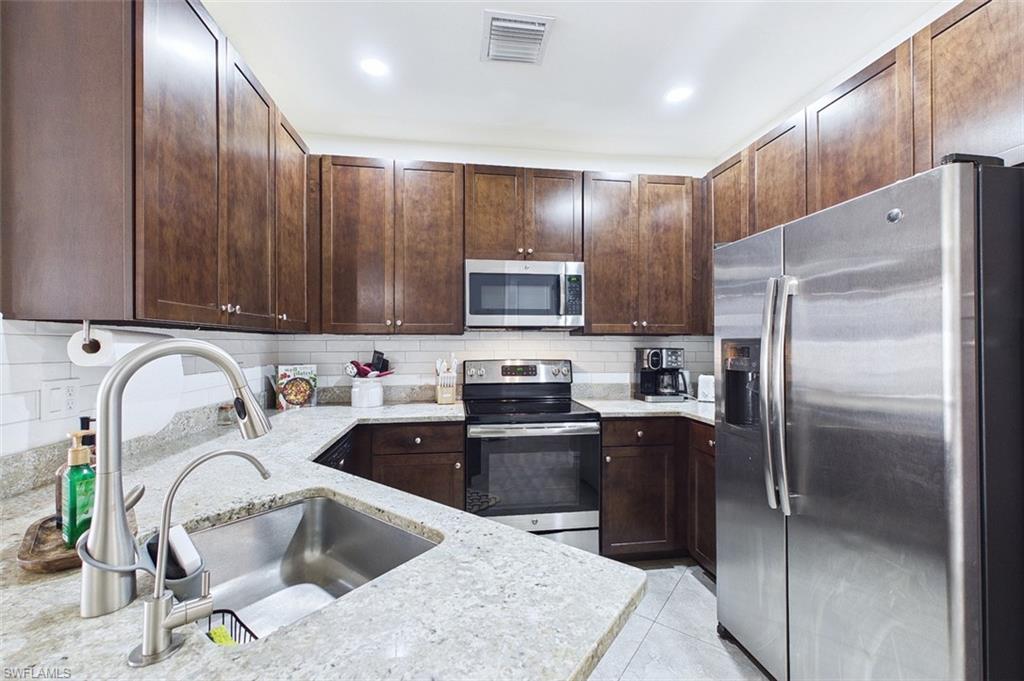 Kitchen featuring stainless steel appliances, tasteful backsplash, light stone counters, and dark brown cabinetry