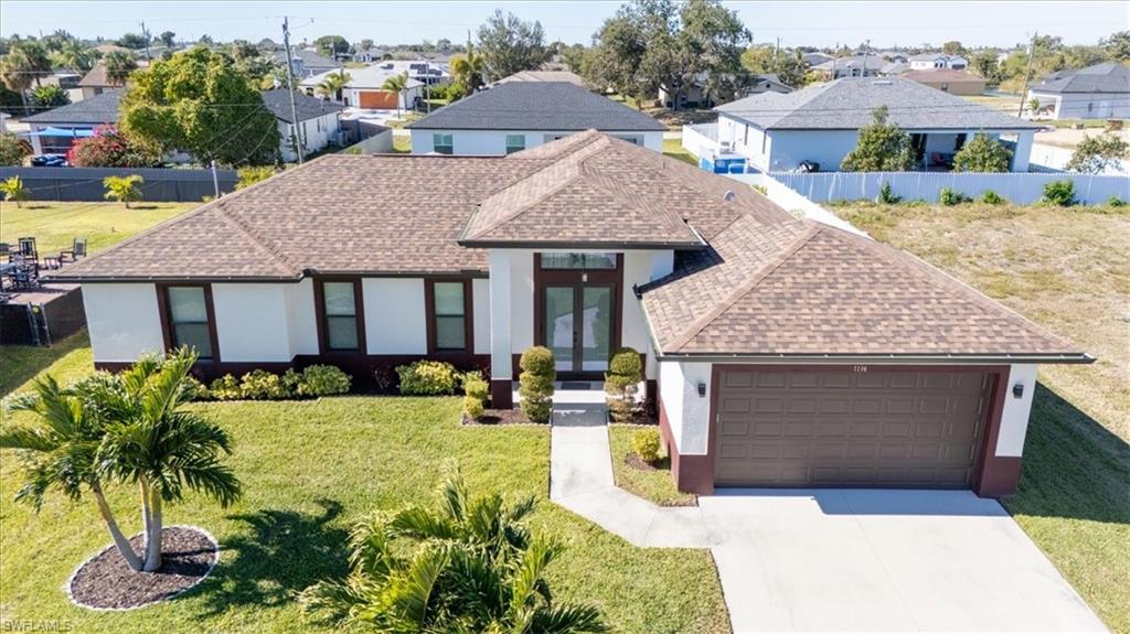 View of front facade with roof with shingles, stucco siding, a front yard, concrete driveway, and french doors