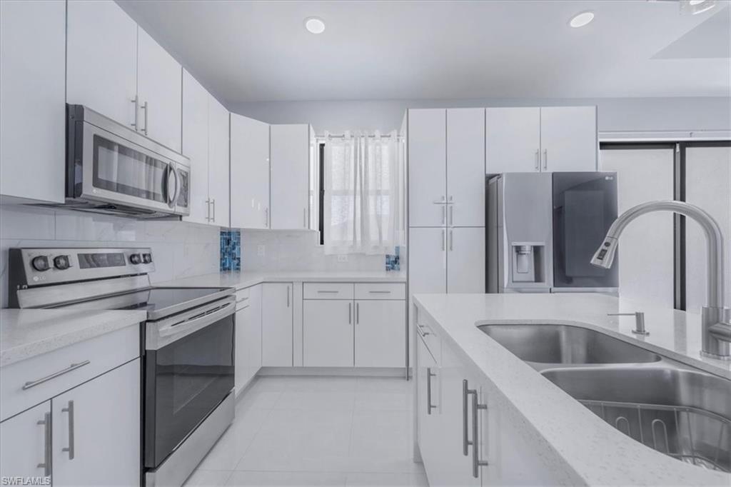 Kitchen with stainless steel appliances, backsplash, light stone countertops, white cabinets, and recessed lighting