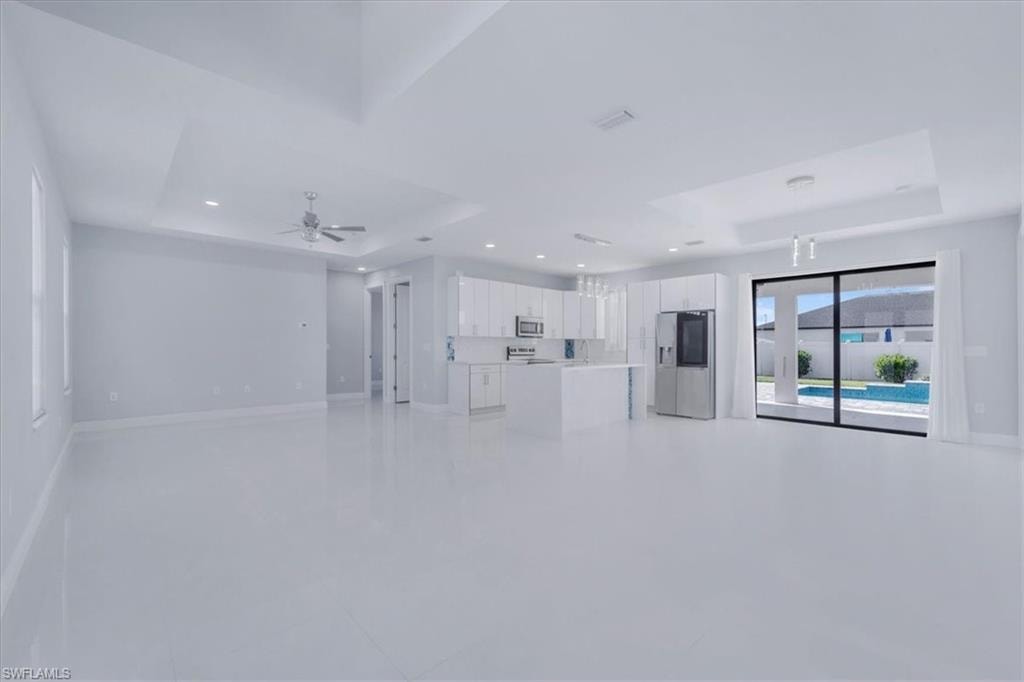 Unfurnished living room with a raised ceiling, recessed lighting, and ceiling fan