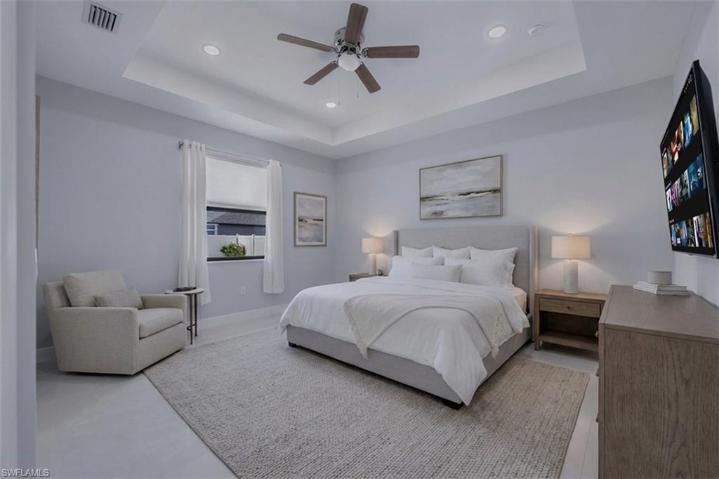 Spacious bedroom featuring light-toned walls, a tray ceiling with recessed lighting and a ceiling fan, and light-toned flooring