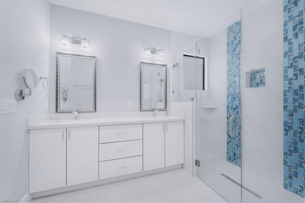 Bathroom featuring a stall shower, double vanity, and light tile patterned flooring