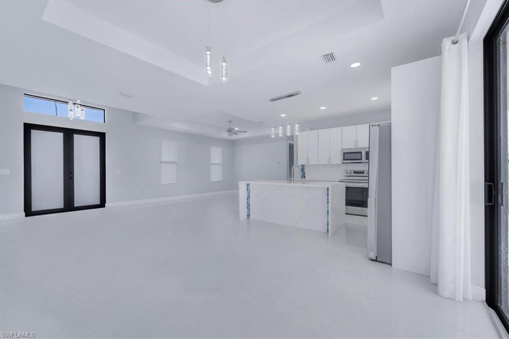 Kitchen featuring pendant lighting, open floor plan, ceiling fan, appliances with stainless steel finishes, and white cabinetry