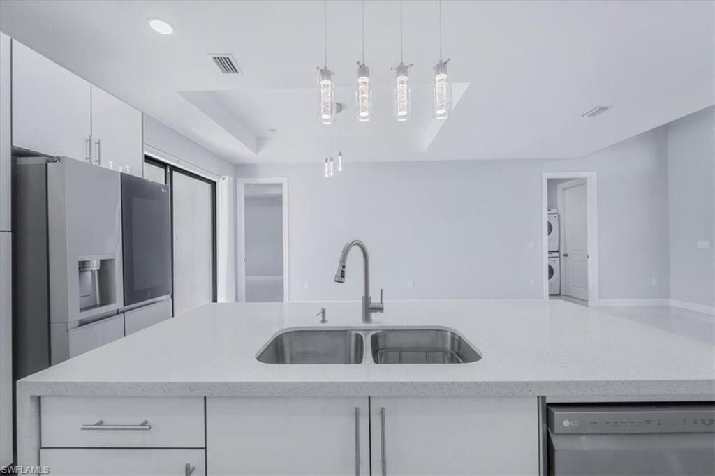 Kitchen featuring light stone countertops, white cabinets, appliances with stainless steel finishes, a center island with sink, and hanging light fixtures