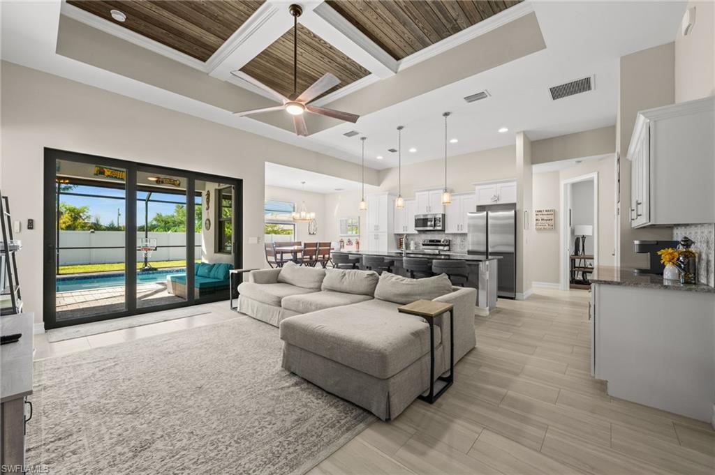 Living room with coffered ceiling, ornamental molding, a chandelier, ceiling fan, and a high ceiling