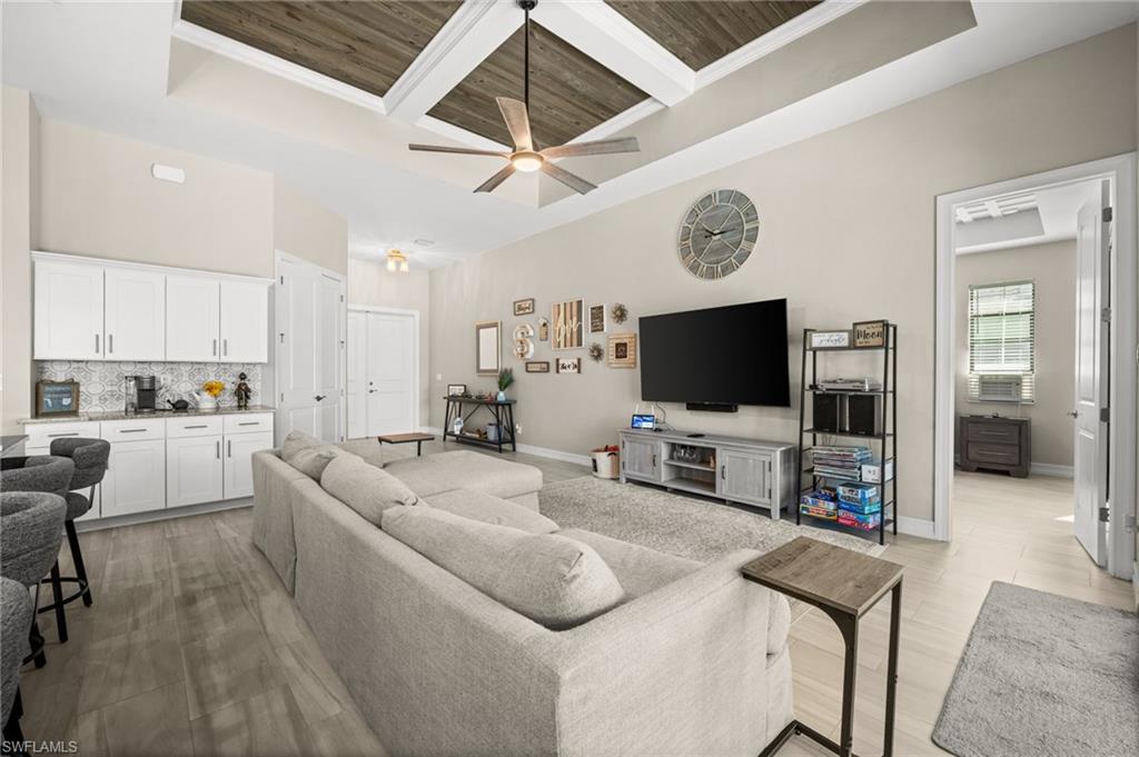 Living room with a wooden ceiling with exposed beams, coffered ceiling, ornamental molding, a ceiling fan, and a raised ceiling