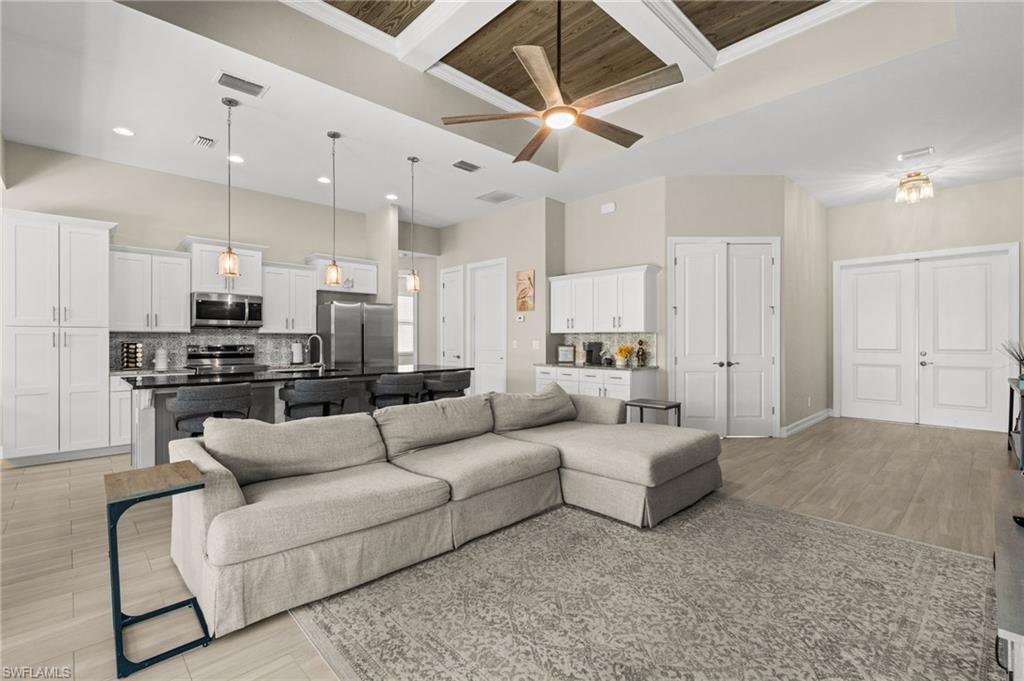 Living room featuring coffered ceiling, beamed ceiling, light wood-style floors, a ceiling fan, and a high ceiling