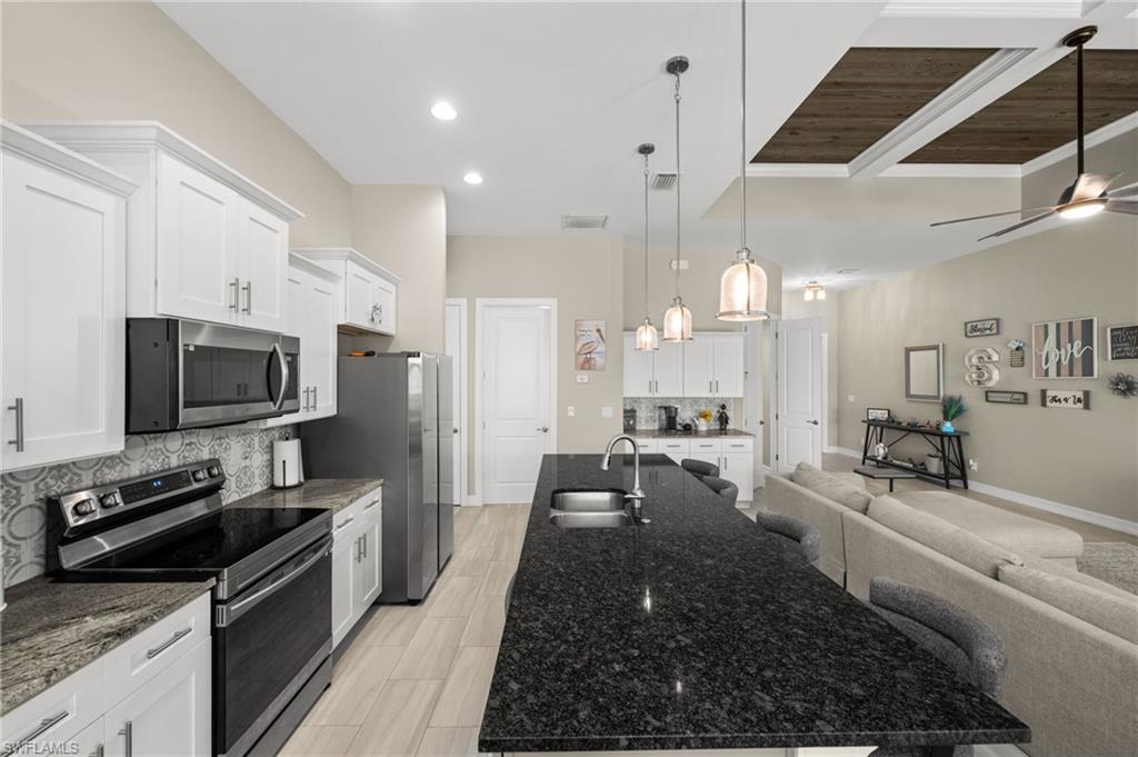 Kitchen with stainless steel appliances, open floor plan, dark stone countertops, white cabinetry, and recessed lighting