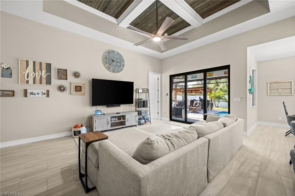 Living room featuring coffered ceiling, a towering ceiling, beamed ceiling, ceiling fan, and wood tiled floors