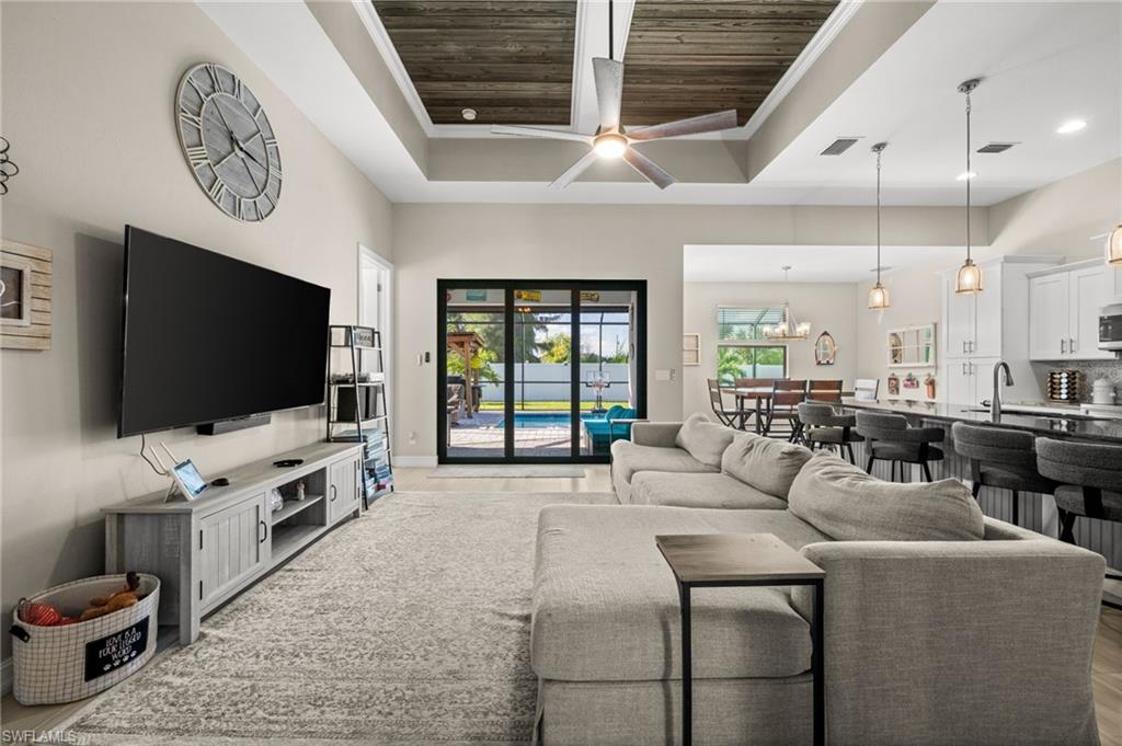 Living room featuring ceiling fan, wooden ceiling, light wood finished floors, crown molding, and a towering ceiling